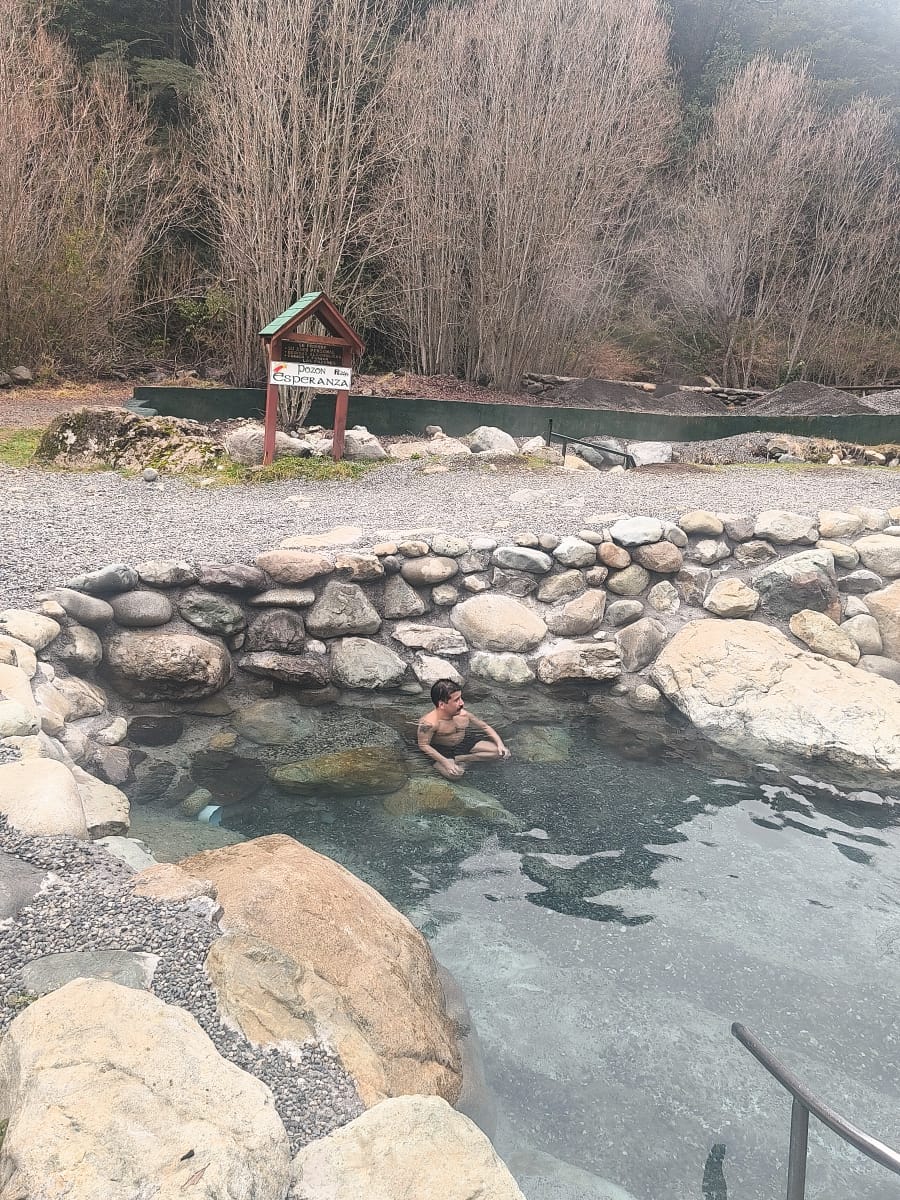 Hombre relajándose en aguas termales rústicas rodeado de exuberante naturaleza